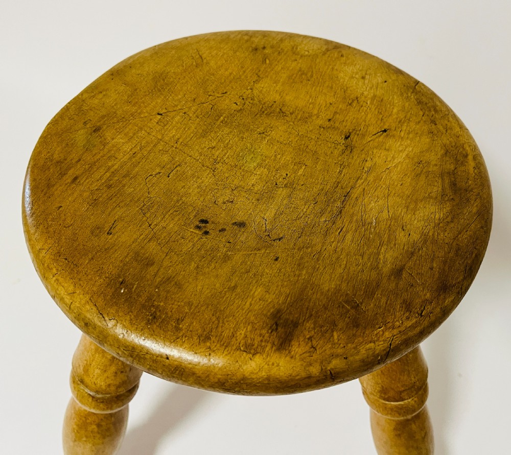 A small antique wooden hearth stool featuring a circular dished seat supported by four splayed turned legs. View II