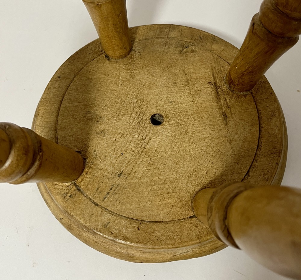 A small antique wooden hearth stool featuring a circular dished seat supported by four splayed turned legs. View V