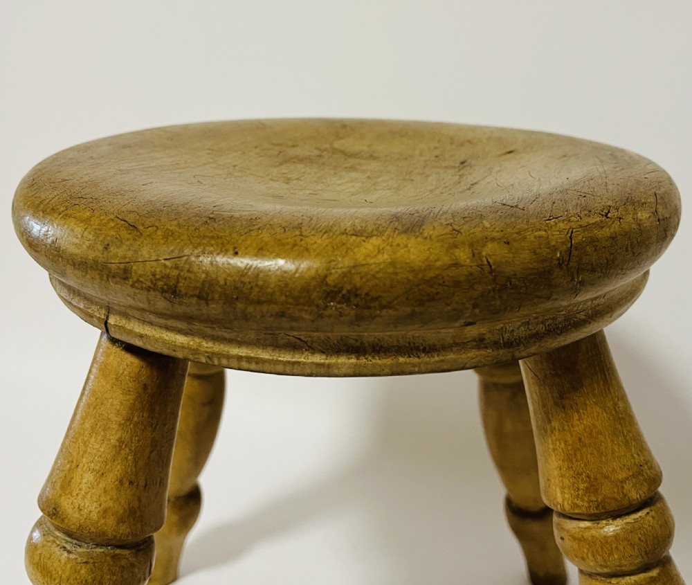 A small antique wooden hearth stool featuring a circular dished seat supported by four splayed turned legs. View VIII