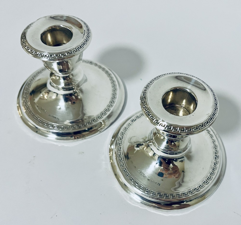 A pair of short Edwardian sterling silver desk candlesticks featuring round bases decorated with engraved Greek key border patterns. View III