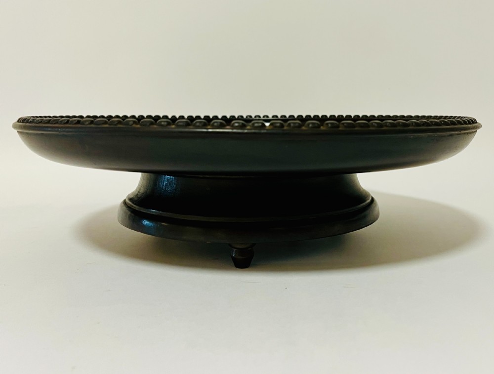 A circular dark wood turned fruit bowl featuring a beaded rim and a raised footed base housing a musical mechanism. View IV