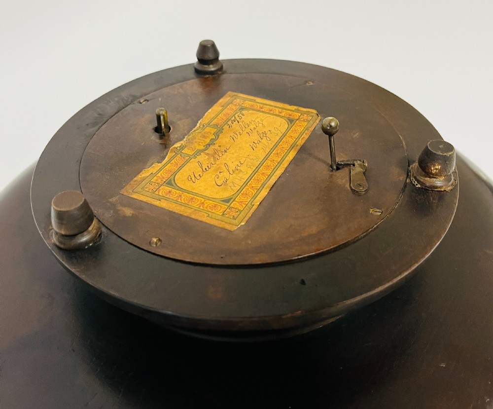 A circular dark wood turned fruit bowl featuring a beaded rim and a raised footed base housing a musical mechanism. View VII