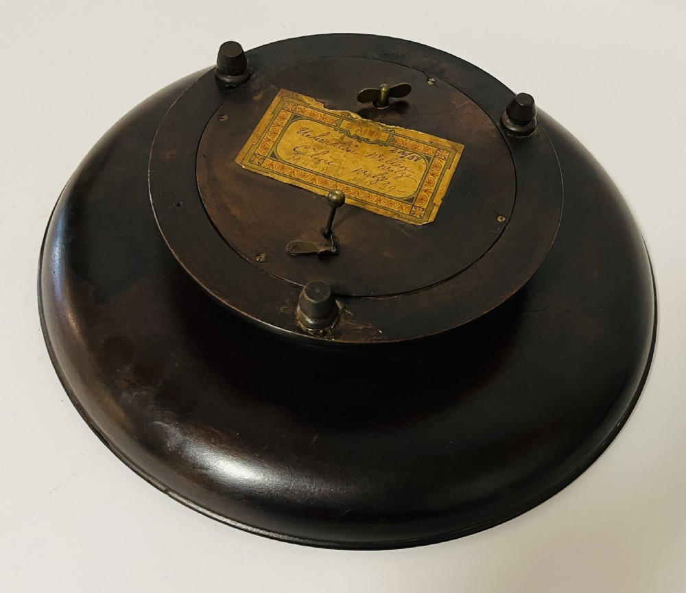 A circular dark wood turned fruit bowl featuring a beaded rim and a raised footed base housing a musical mechanism. View IX