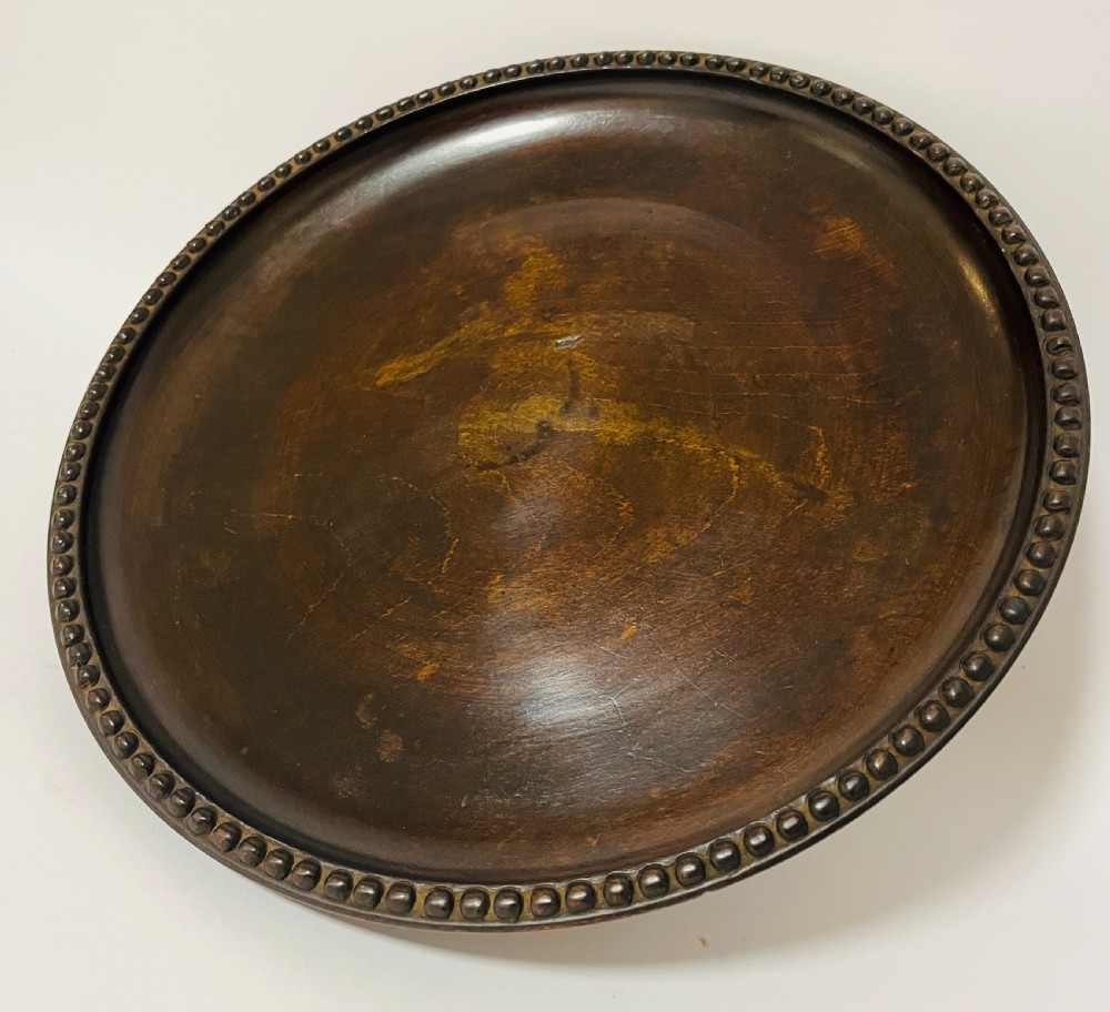 A circular dark wood turned fruit bowl featuring a beaded rim and a raised footed base housing a musical mechanism. View X