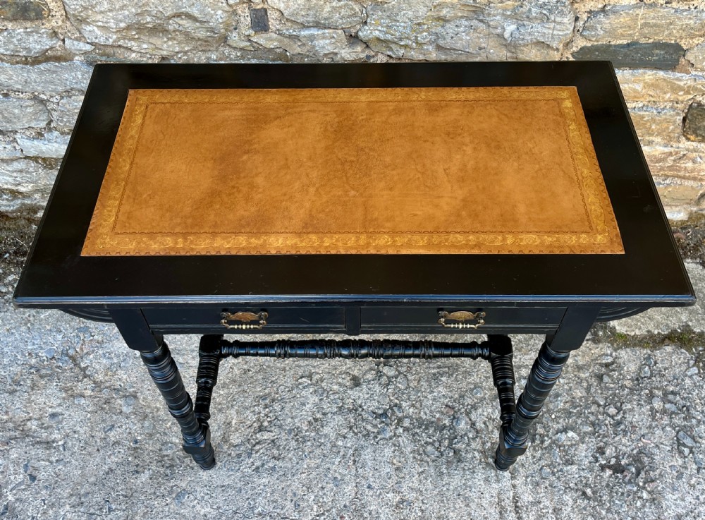 An Aesthetic Movement ebonised writing desk with a tan leather inset top, two frieze drawers with brass handles, and turned spindle legs. View IV