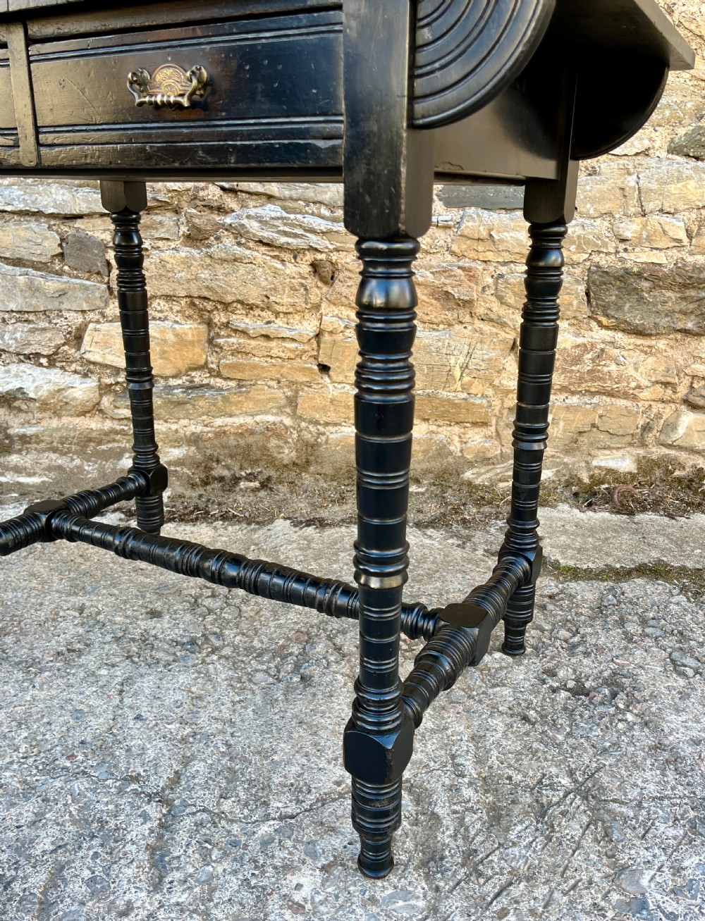 An Aesthetic Movement ebonised writing desk with a tan leather inset top, two frieze drawers with brass handles, and turned spindle legs. View VI