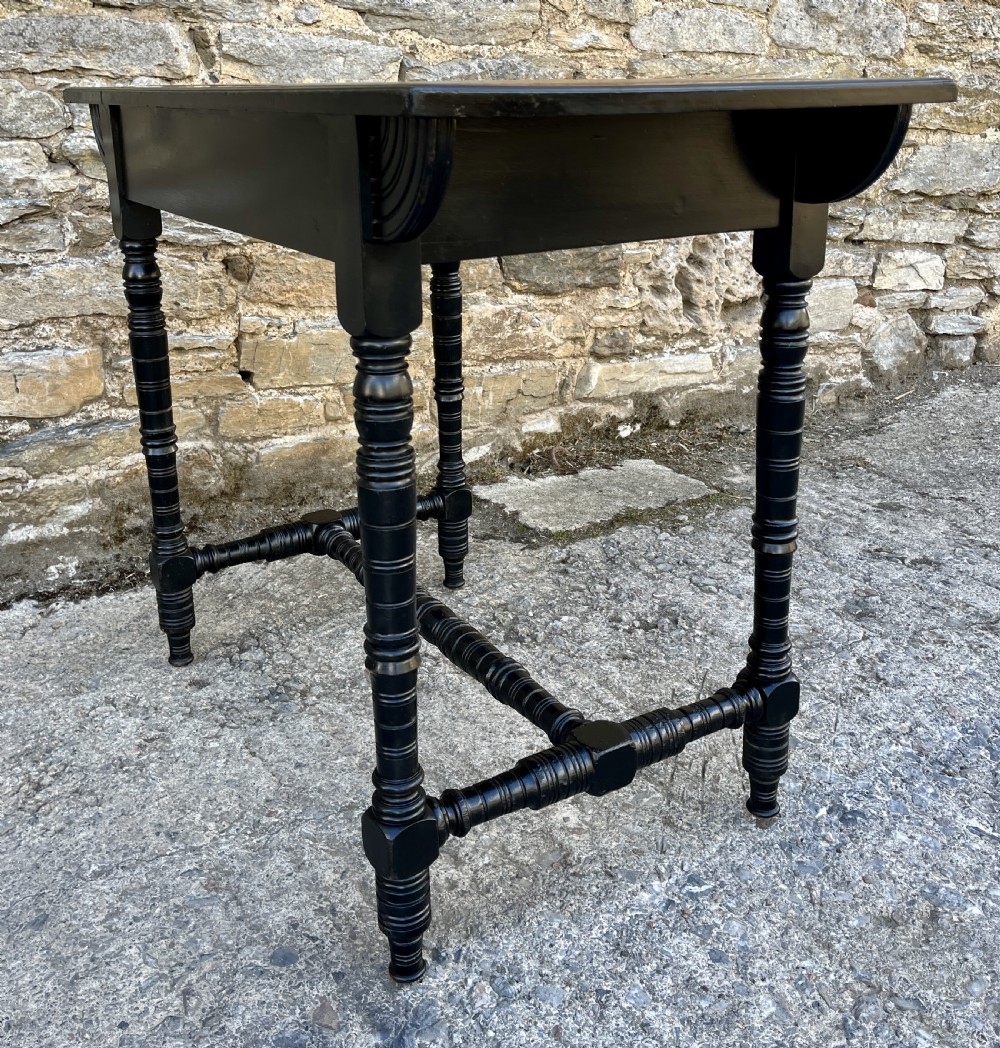 An Aesthetic Movement ebonised writing desk with a tan leather inset top, two frieze drawers with brass handles, and turned spindle legs. View X
