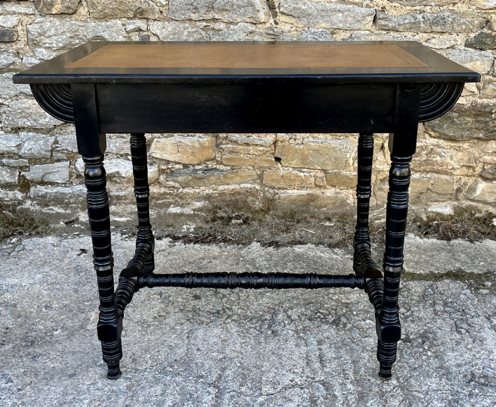 An Aesthetic Movement ebonised writing desk with a tan leather inset top, two frieze drawers with brass handles, and turned spindle legs. View XII
