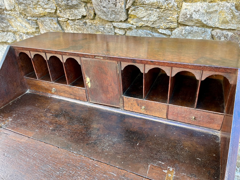 An antique dark oak Georgian bureau featuring a slant front, ornate brass escutcheons, lopers, and bracket feet. View VII
