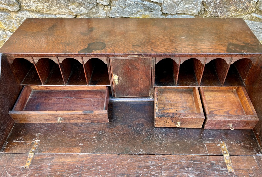 An antique dark oak Georgian bureau featuring a slant front, ornate brass escutcheons, lopers, and bracket feet. View IX