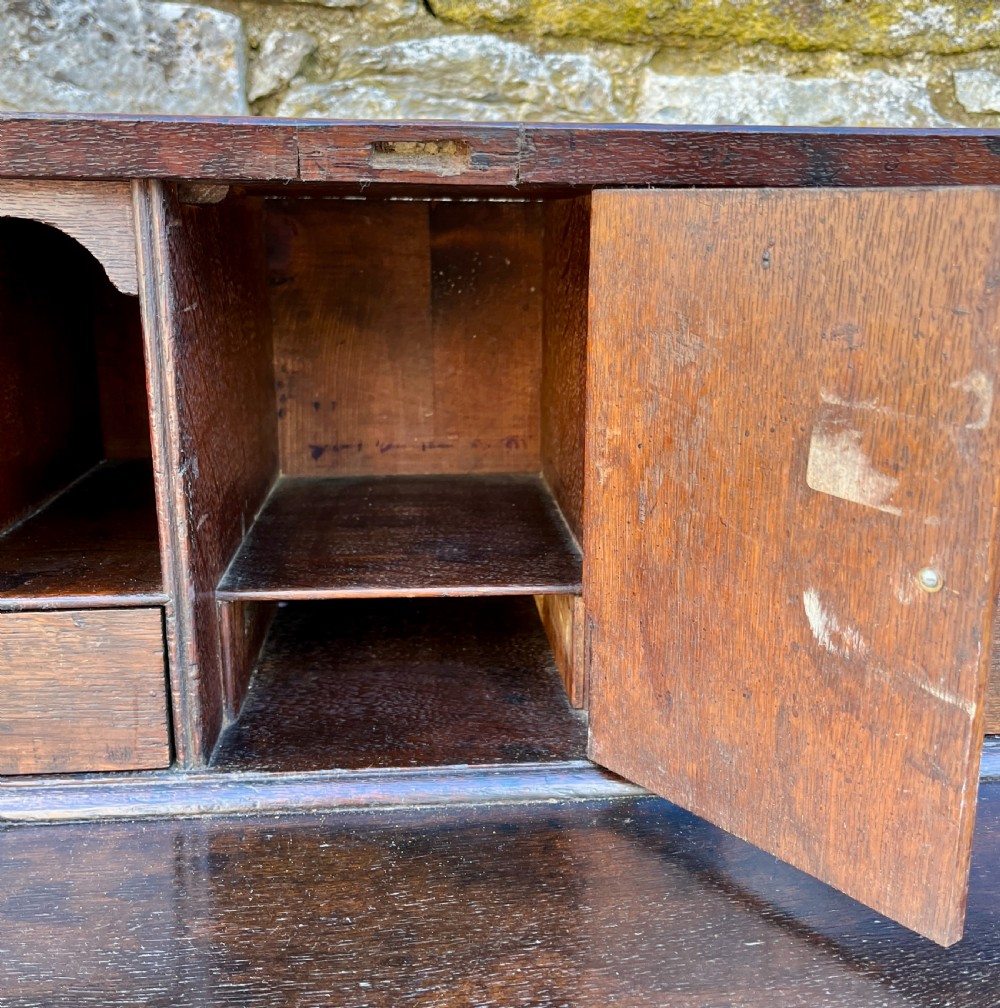 An antique dark oak Georgian bureau featuring a slant front, ornate brass escutcheons, lopers, and bracket feet. View X