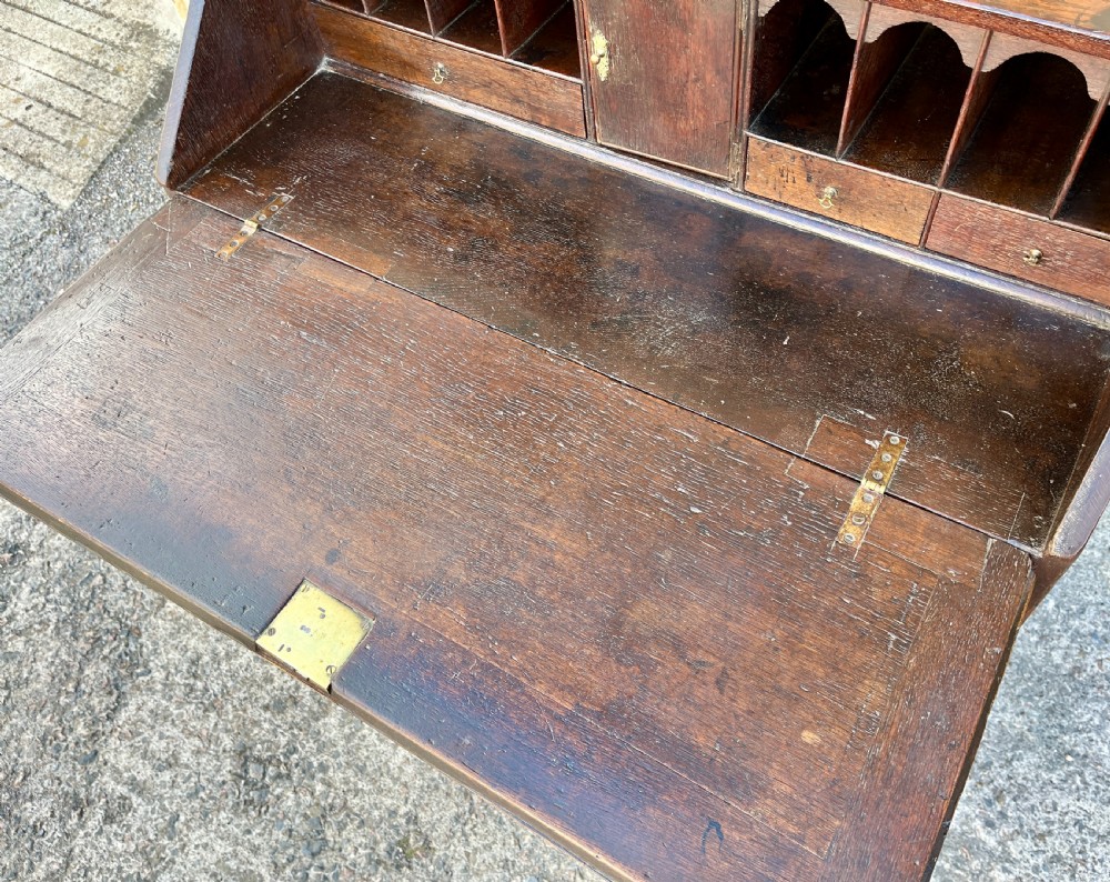 An antique dark oak Georgian bureau featuring a slant front, ornate brass escutcheons, lopers, and bracket feet. View XI