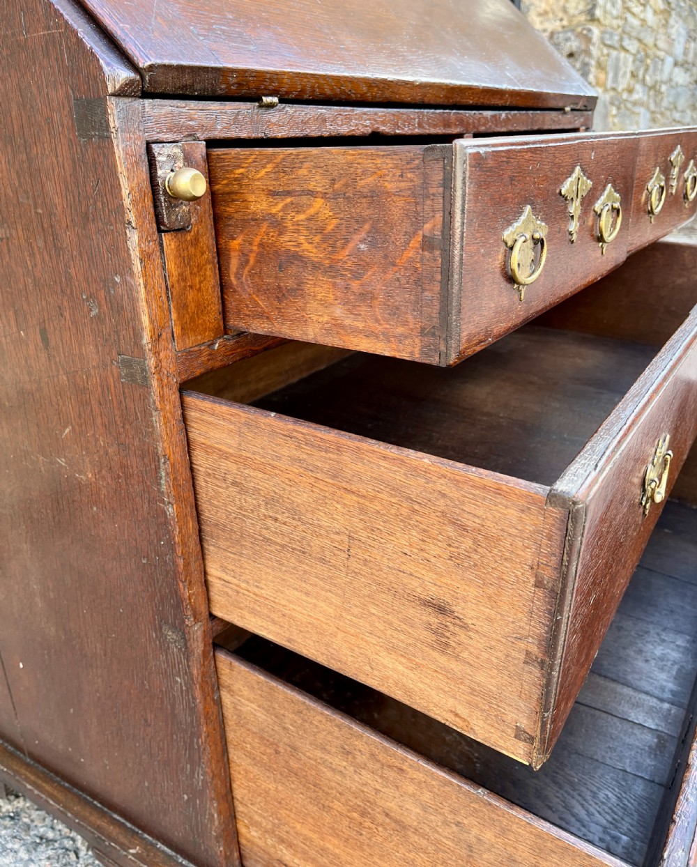 An antique dark oak Georgian bureau featuring a slant front, ornate brass escutcheons, lopers, and bracket feet. View XIV