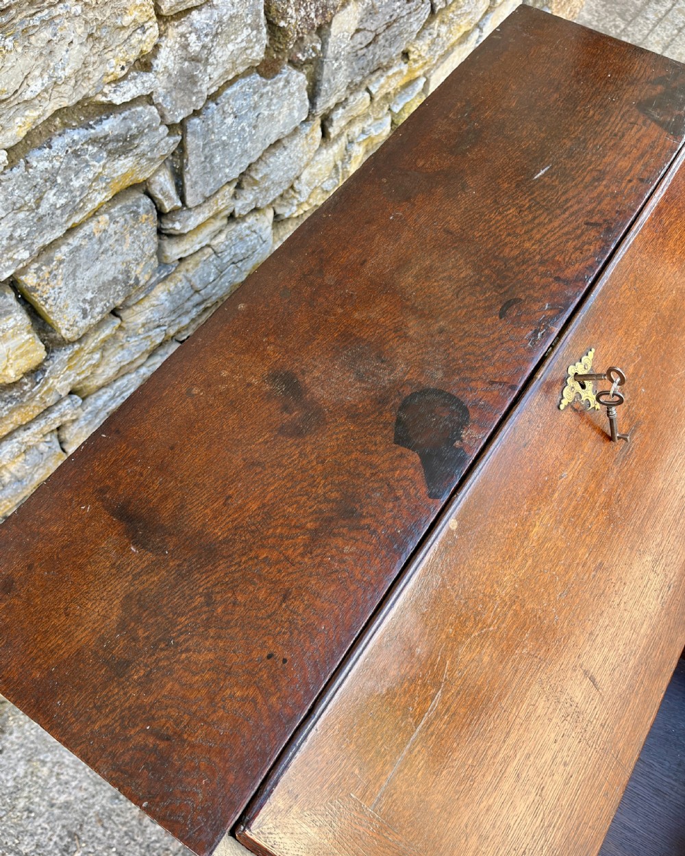 An antique dark oak Georgian bureau featuring a slant front, ornate brass escutcheons, lopers, and bracket feet. View XV