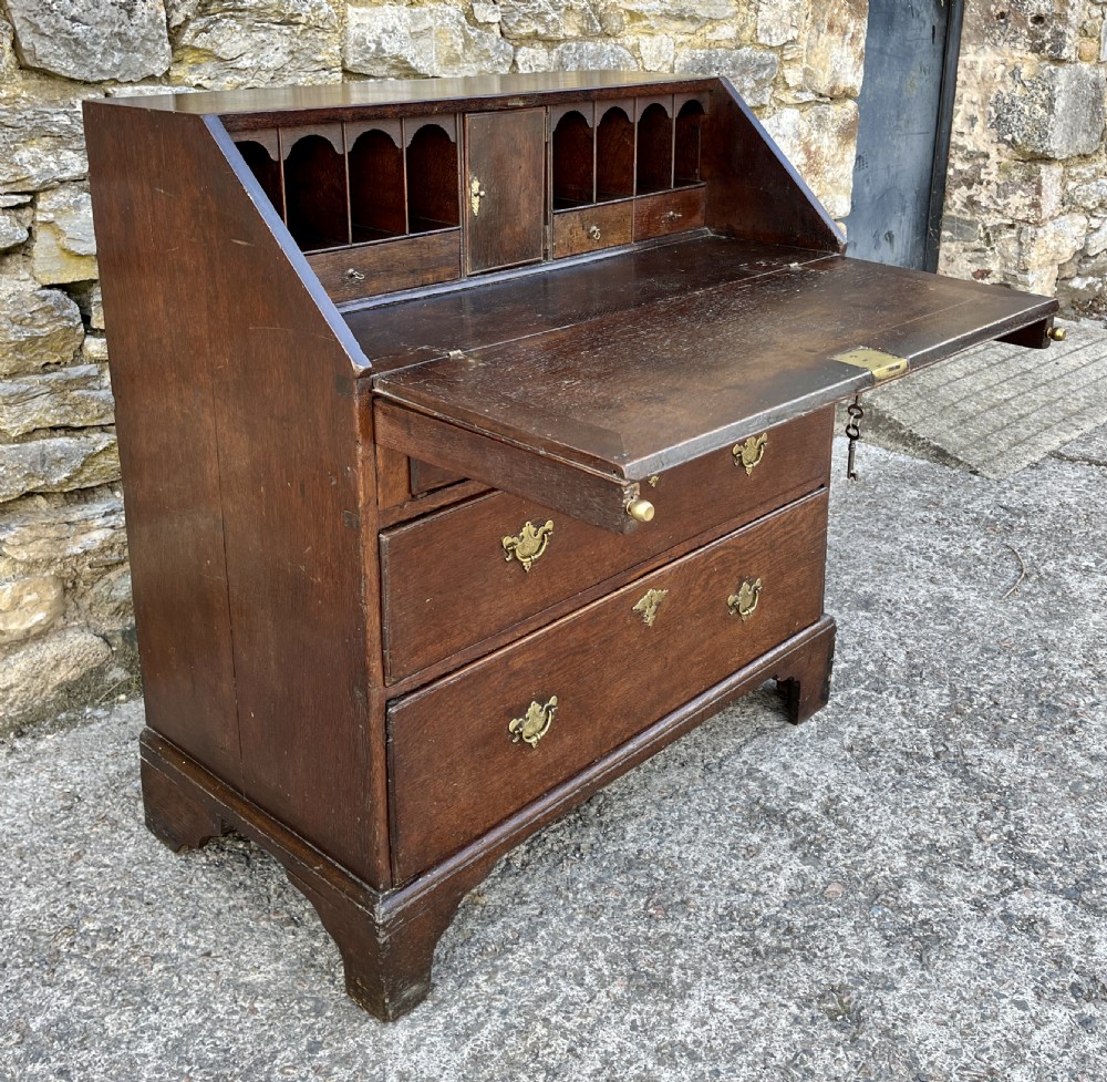 An antique dark oak Georgian bureau featuring a slant front, ornate brass escutcheons, lopers, and bracket feet. View XVII