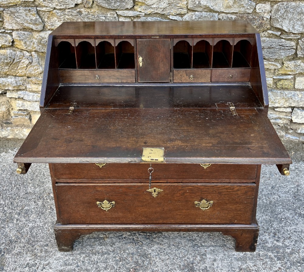 An antique dark oak Georgian bureau featuring a slant front, ornate brass escutcheons, lopers, and bracket feet. View XIX