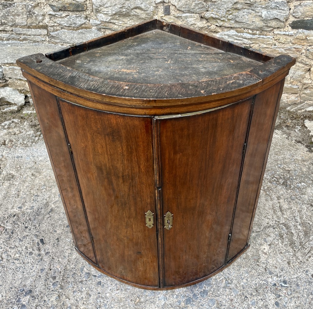 A Georgian bow-fronted mahogany hanging corner cupboard with twin doors and decorative brass escutcheons. View II