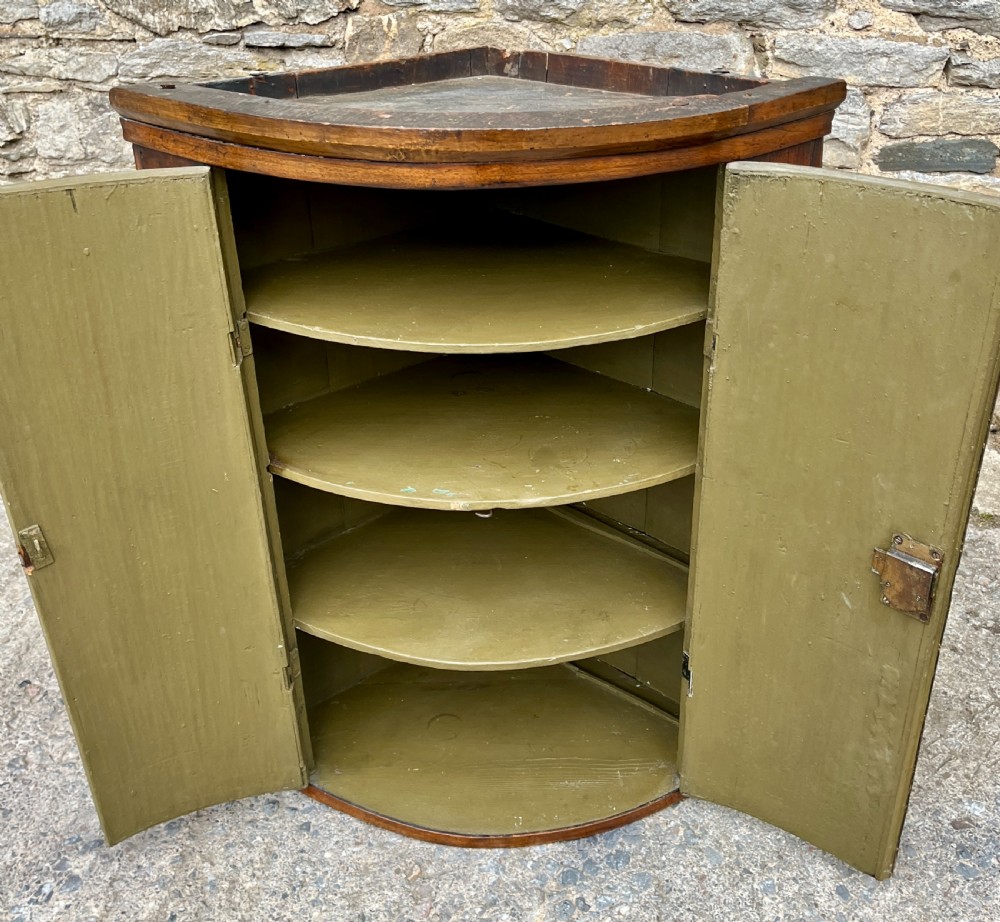 A Georgian bow-fronted mahogany hanging corner cupboard with twin doors and decorative brass escutcheons. View VI