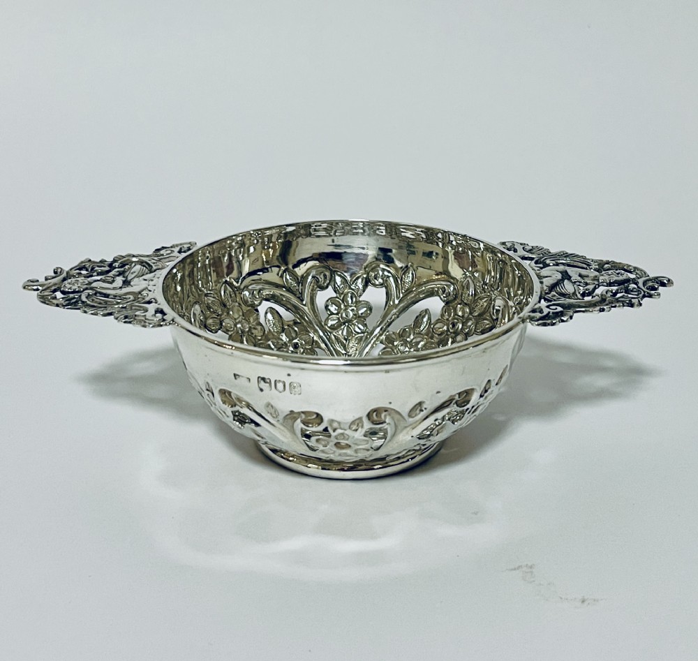 An Edwardian sterling silver quaich featuring intricate pierced floral sides, two ornate cast scroll handles, and hallmarks visible on the bowl.