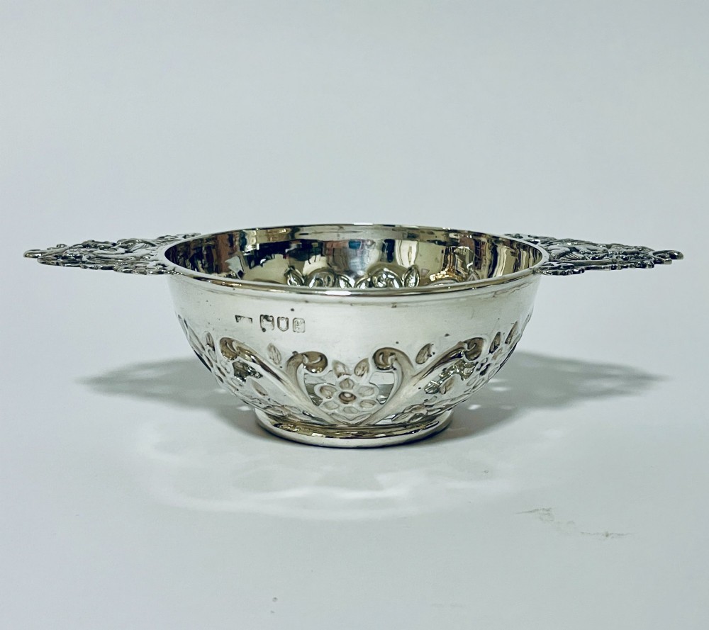 An Edwardian sterling silver quaich featuring intricate pierced floral sides, two ornate cast scroll handles, and hallmarks visible on the bowl. View II