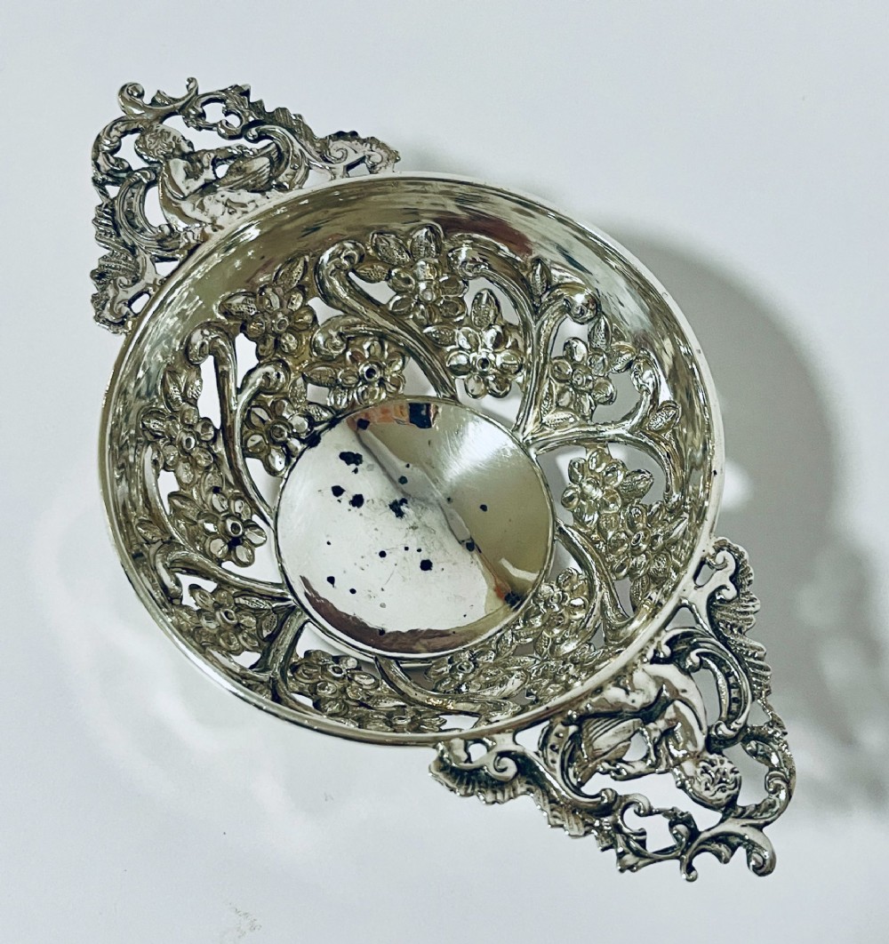 An Edwardian sterling silver quaich featuring intricate pierced floral sides, two ornate cast scroll handles, and hallmarks visible on the bowl. View III