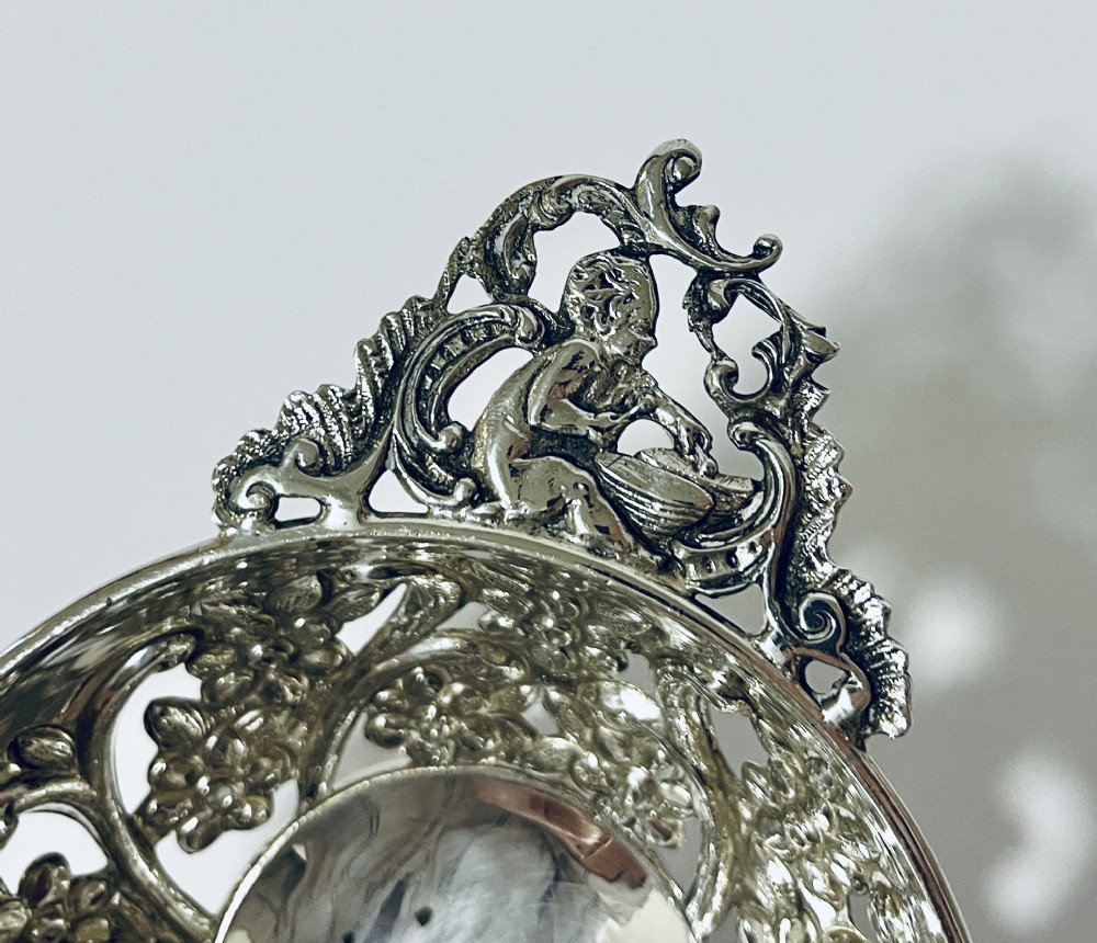 An Edwardian sterling silver quaich featuring intricate pierced floral sides, two ornate cast scroll handles, and hallmarks visible on the bowl. View IV