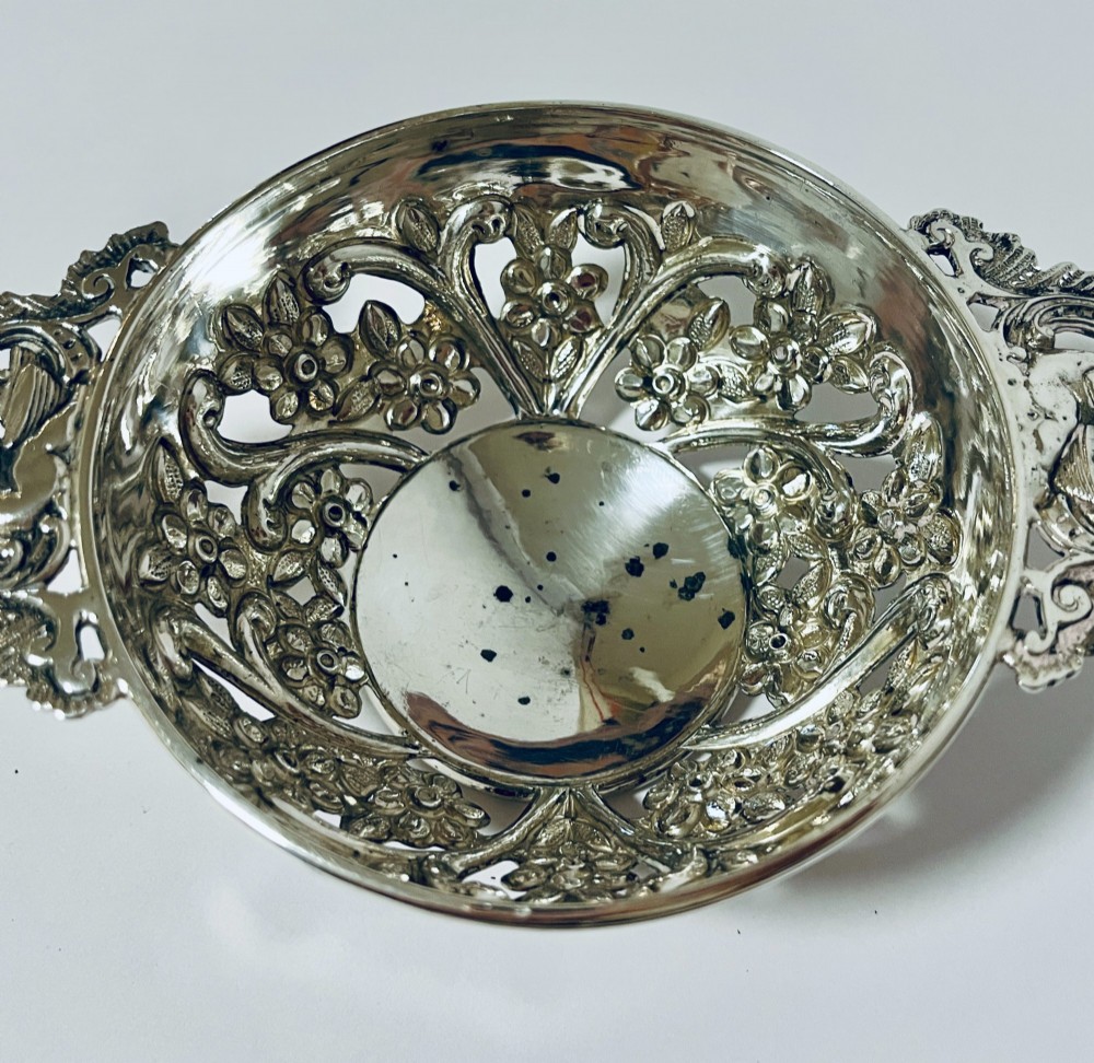 An Edwardian sterling silver quaich featuring intricate pierced floral sides, two ornate cast scroll handles, and hallmarks visible on the bowl. View V