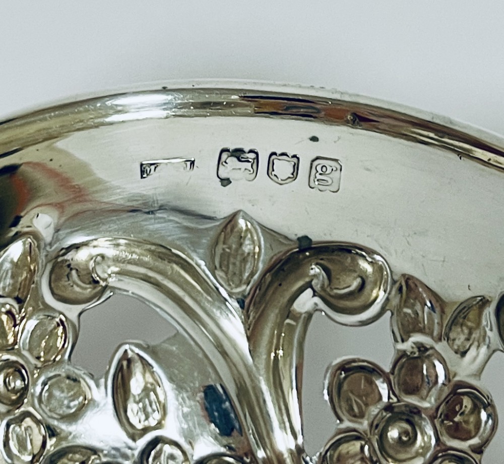 An Edwardian sterling silver quaich featuring intricate pierced floral sides, two ornate cast scroll handles, and hallmarks visible on the bowl. View VII