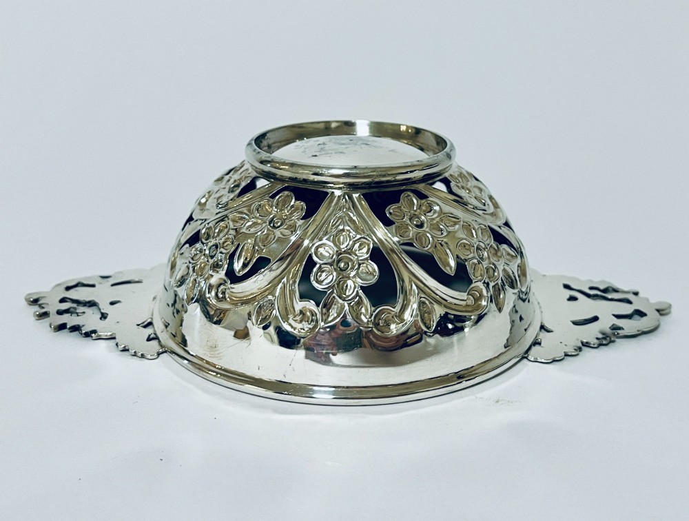 An Edwardian sterling silver quaich featuring intricate pierced floral sides, two ornate cast scroll handles, and hallmarks visible on the bowl. View VIII
