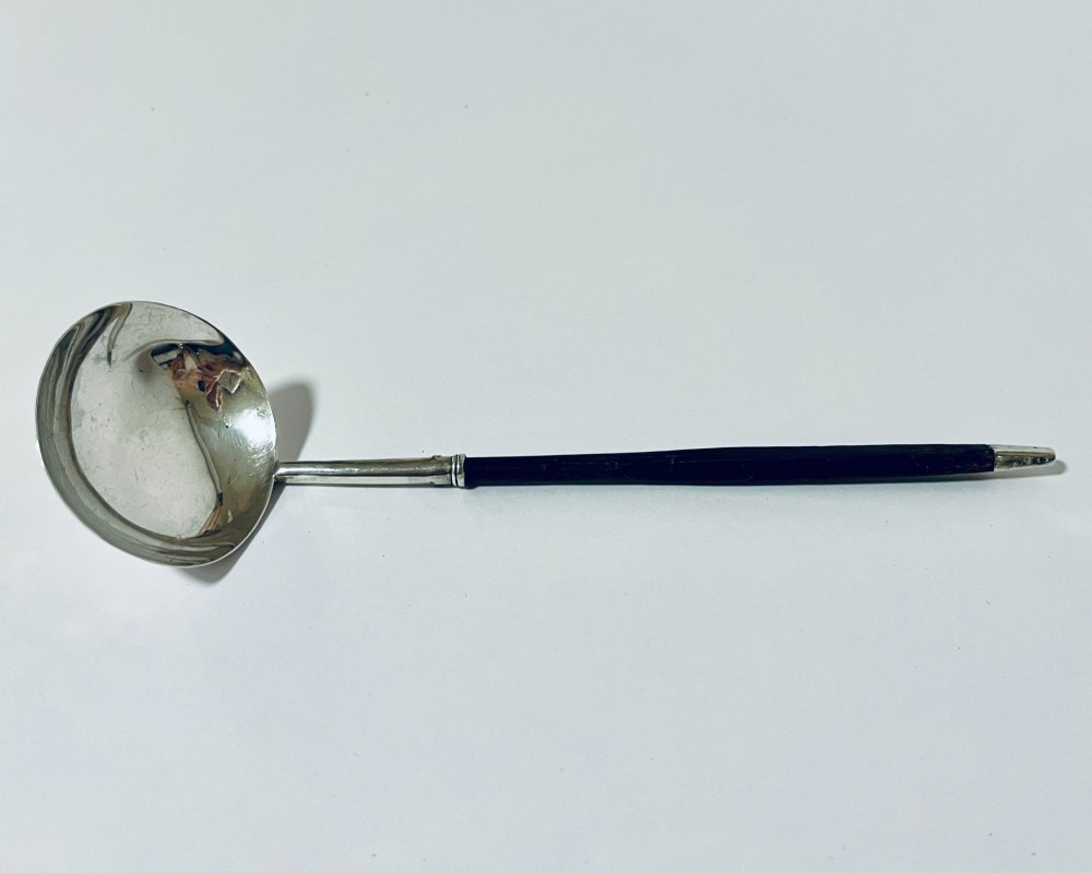 A Georgian Irish silver punch ladle with a circular polished silver bowl and a long turned dark wooden handle.