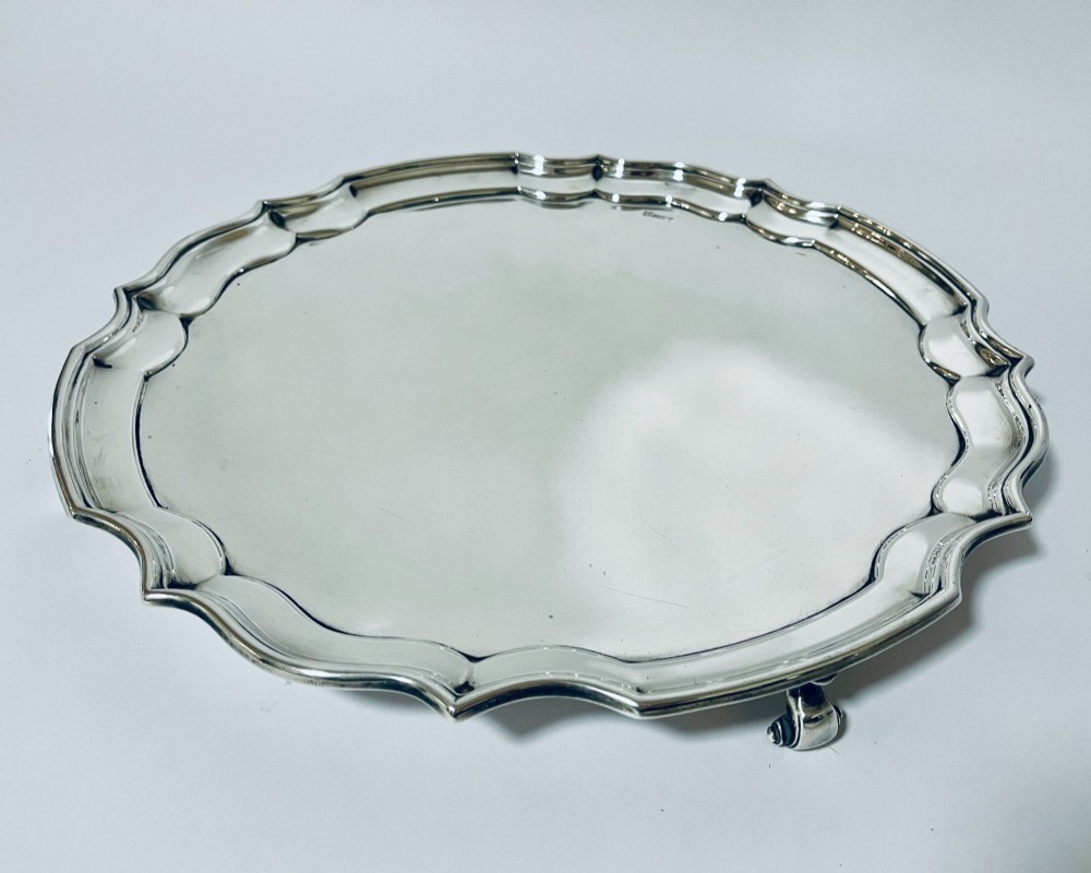 An antique circular silver salver with a moulded piecrust border and raised scroll feet, photographed on a plain white background. View II