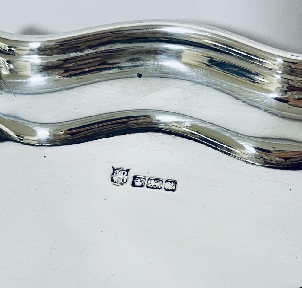 An antique circular silver salver with a moulded piecrust border and raised scroll feet, photographed on a plain white background. View III
