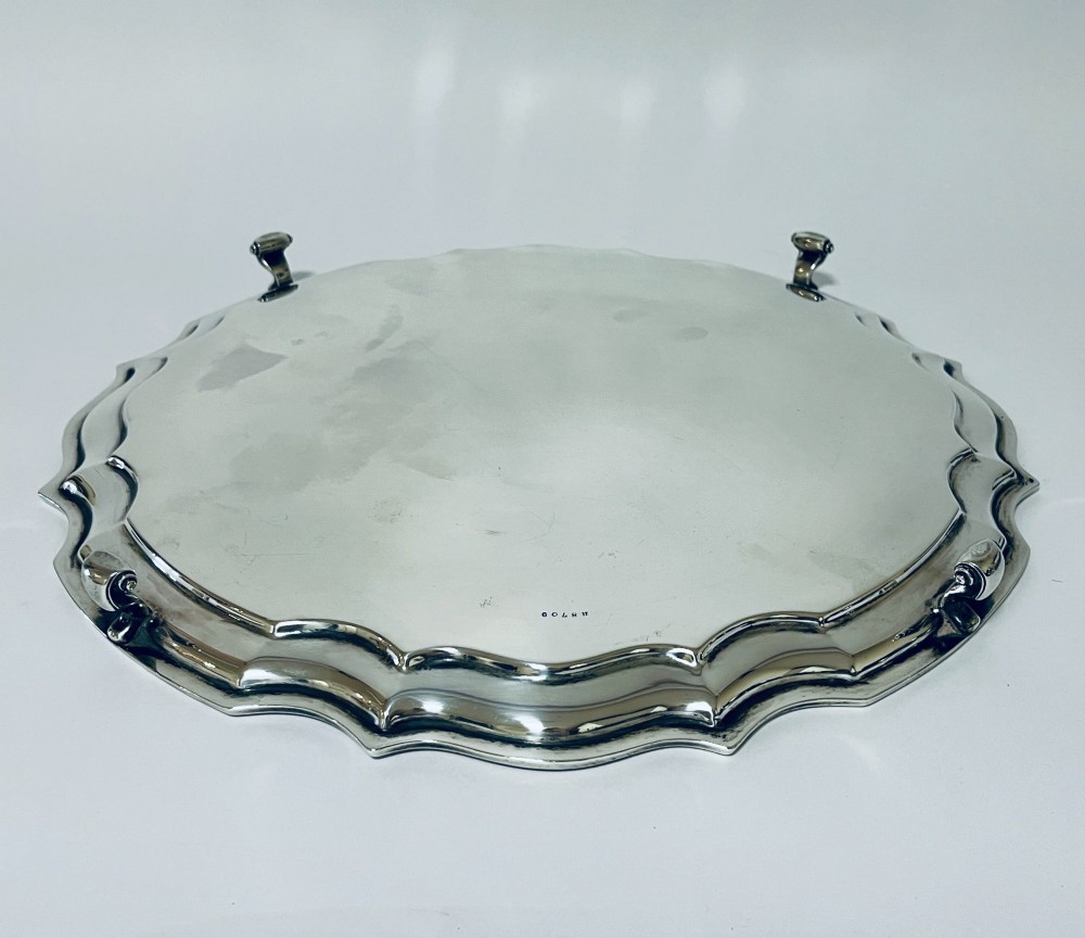 An antique circular silver salver with a moulded piecrust border and raised scroll feet, photographed on a plain white background. View V