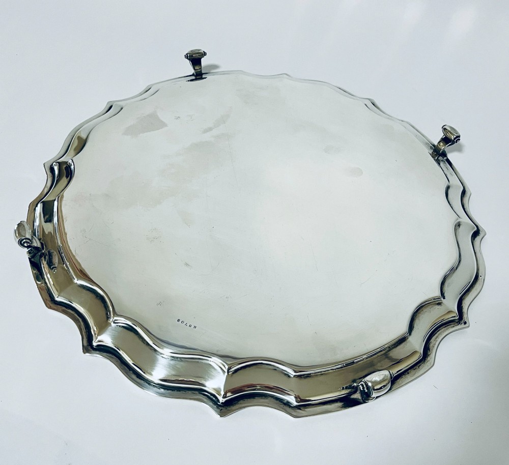 An antique circular silver salver with a moulded piecrust border and raised scroll feet, photographed on a plain white background. View VI