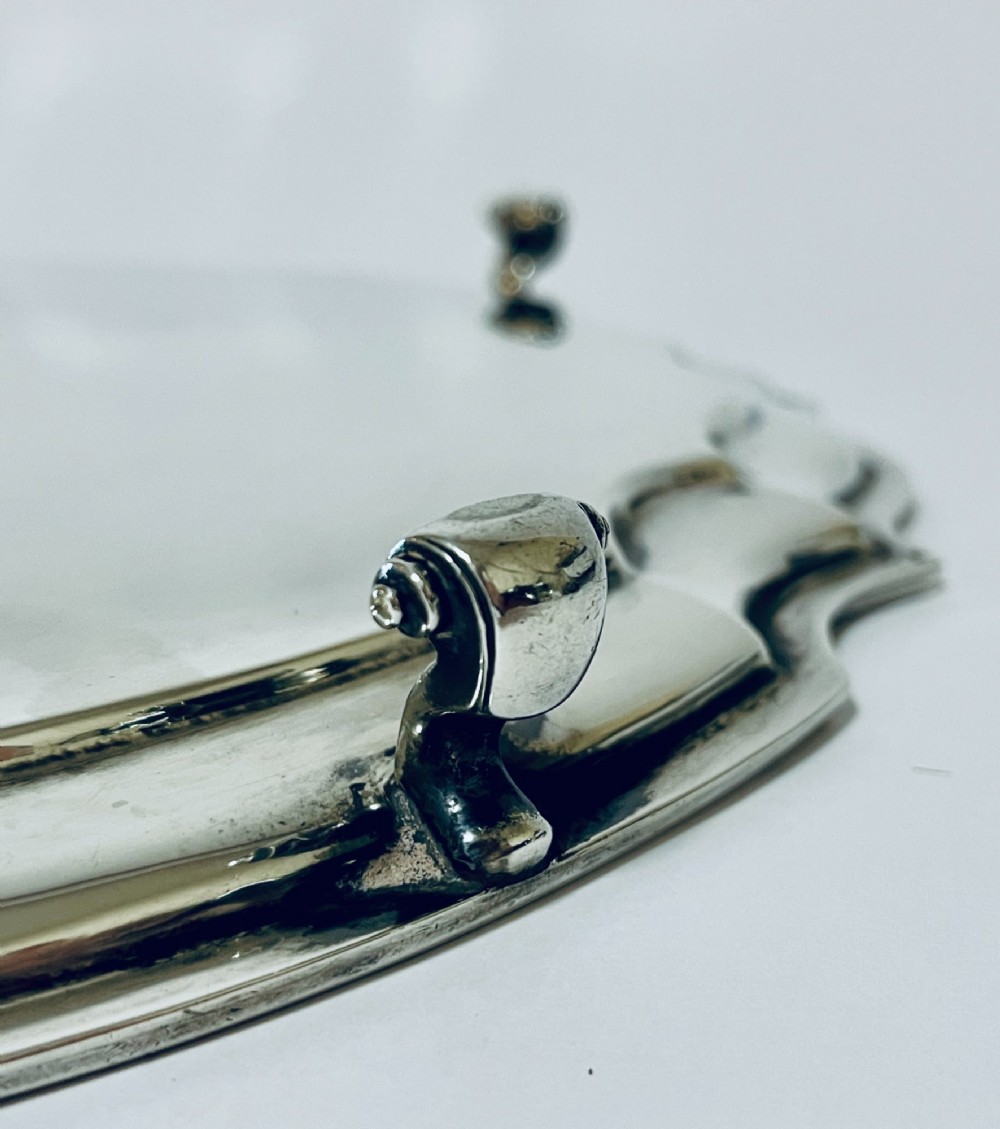 An antique circular silver salver with a moulded piecrust border and raised scroll feet, photographed on a plain white background. View VII
