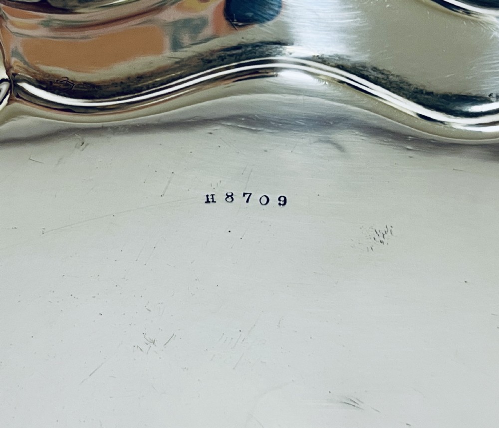 An antique circular silver salver with a moulded piecrust border and raised scroll feet, photographed on a plain white background. View VIII