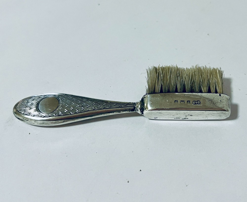 An antique silver moustache brush featuring a textured handle with a central circular cartouche and visible silver hallmarks stamped on the brush head. View III