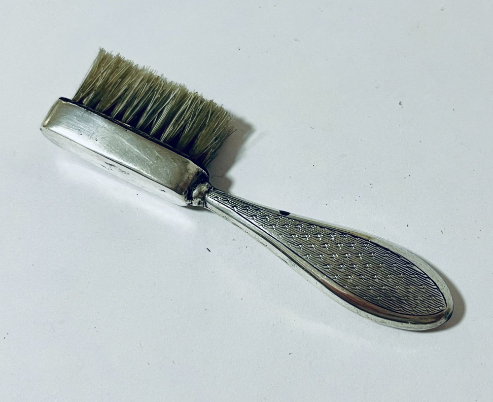 An antique silver moustache brush featuring a textured handle with a central circular cartouche and visible silver hallmarks stamped on the brush head. View VI
