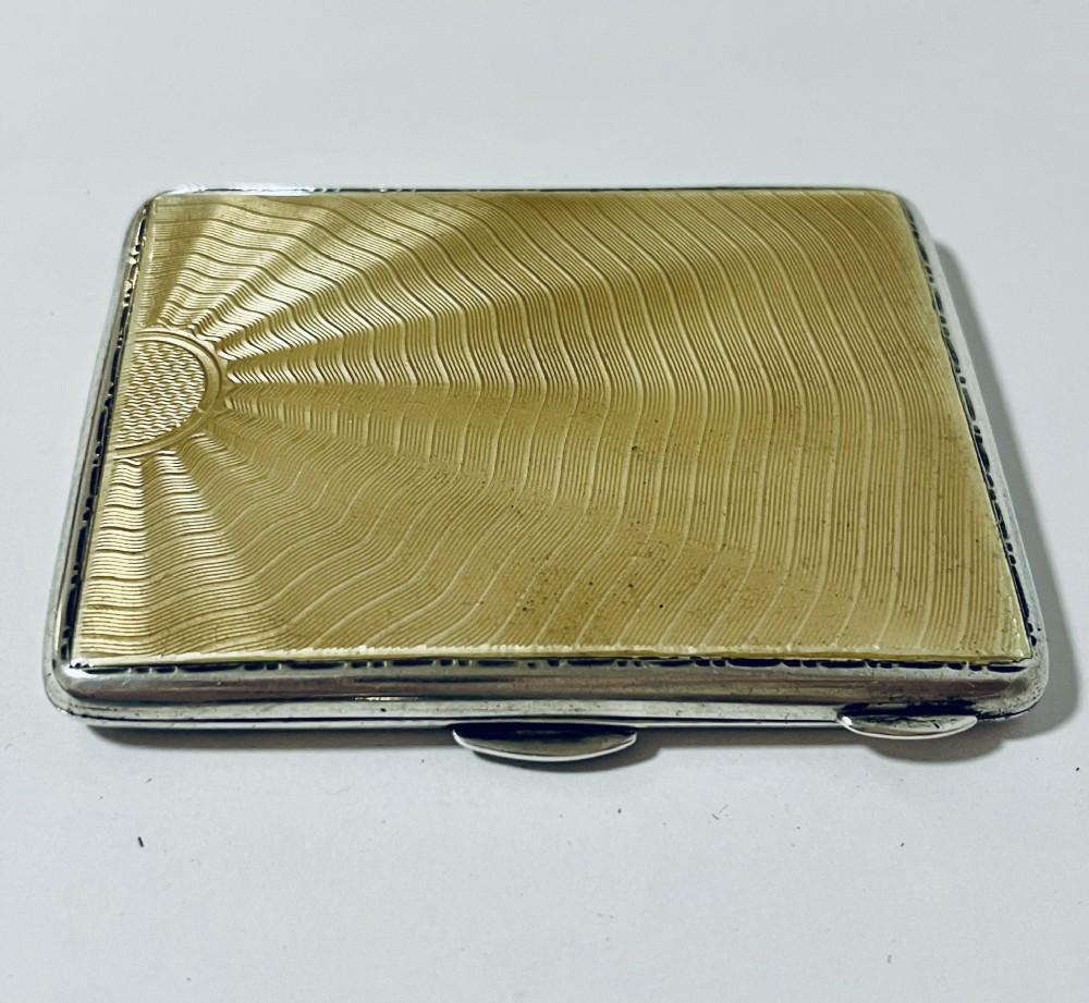 An Art Deco rectangular silver cigarette case featuring a pale yellow translucent enamel panel over a sunburst guilloche pattern.