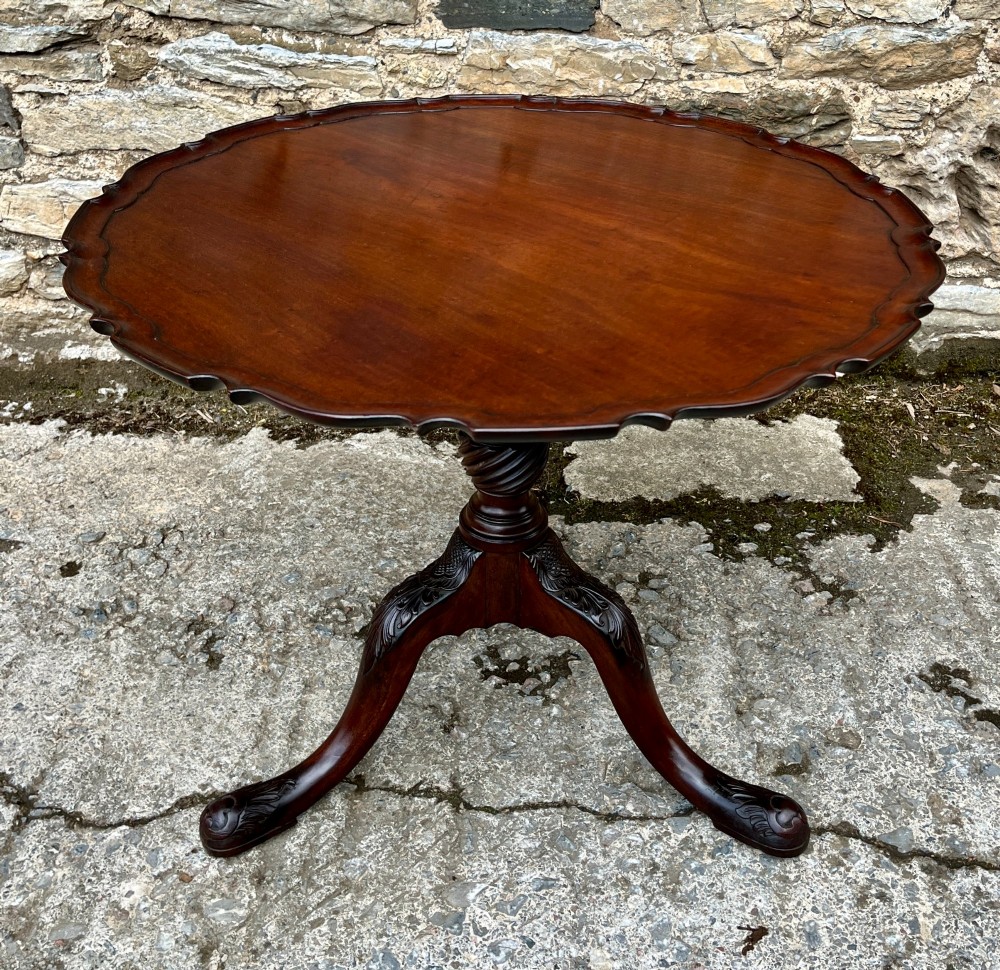 A Georgian mahogany tilt-top side table featuring a scalloped pie-crust edge, turned central column, and carved tripod cabriole legs.