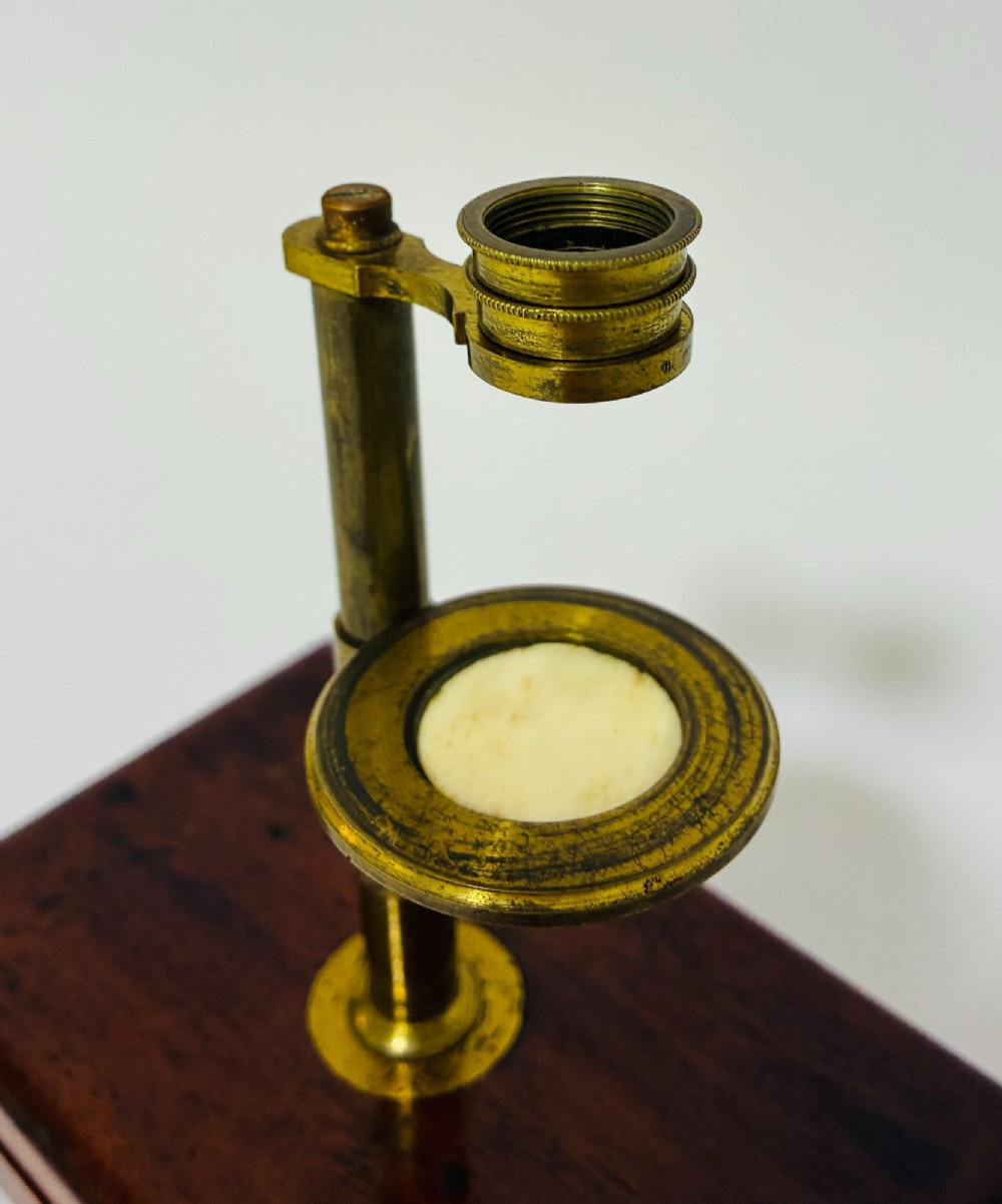 A 19th-century brass botanical field microscope mounted upright on a polished mahogany wooden storage box base. View II