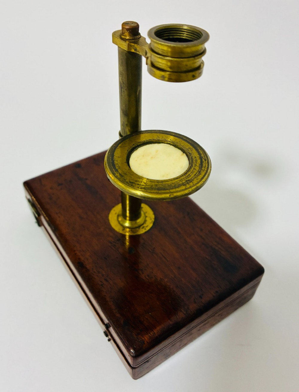 A 19th-century brass botanical field microscope mounted upright on a polished mahogany wooden storage box base. View III