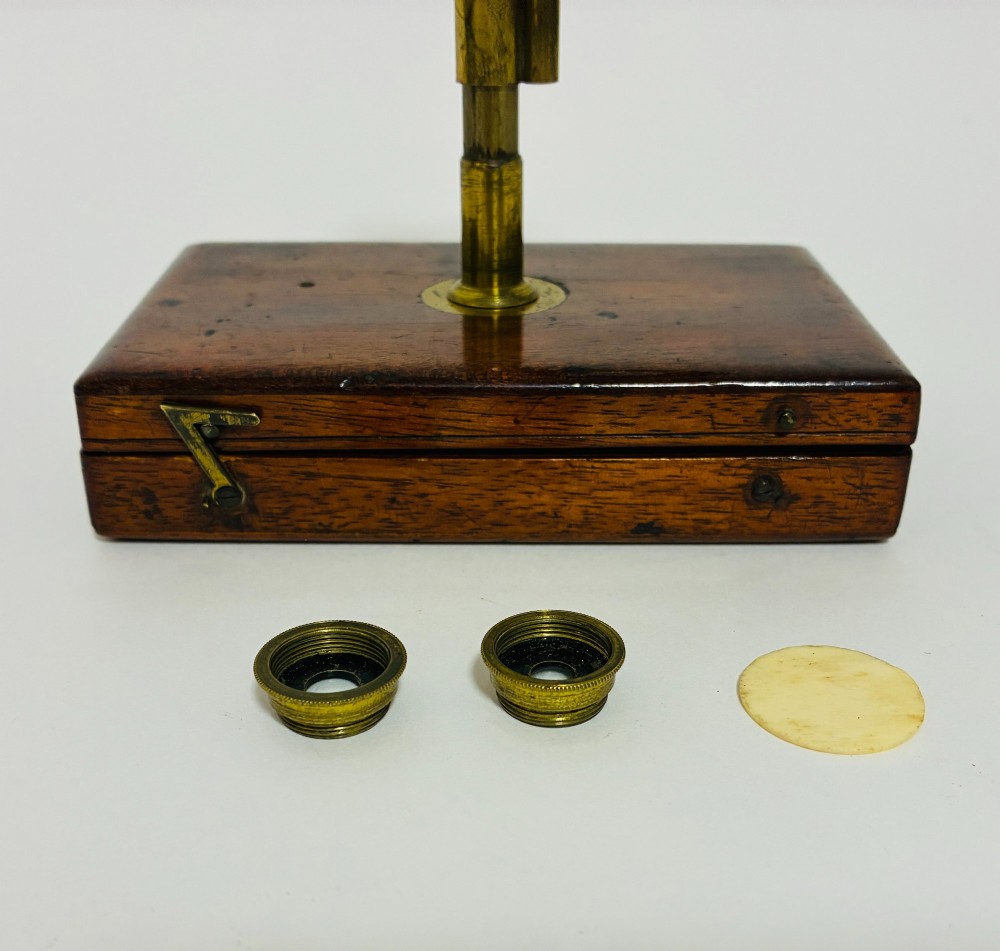 A 19th-century brass botanical field microscope mounted upright on a polished mahogany wooden storage box base. View IV