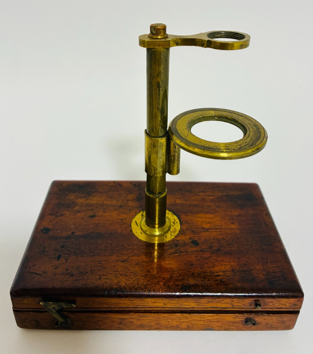 A 19th-century brass botanical field microscope mounted upright on a polished mahogany wooden storage box base. View V