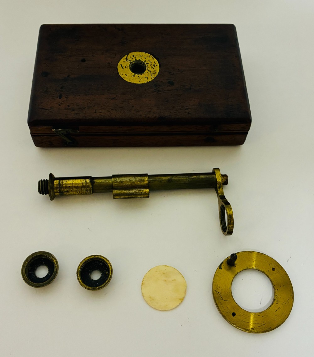 A 19th-century brass botanical field microscope mounted upright on a polished mahogany wooden storage box base. View VI