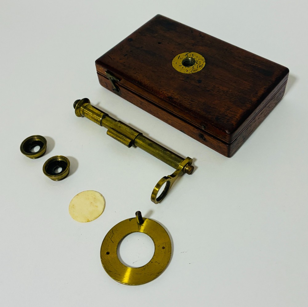 A 19th-century brass botanical field microscope mounted upright on a polished mahogany wooden storage box base. View VII