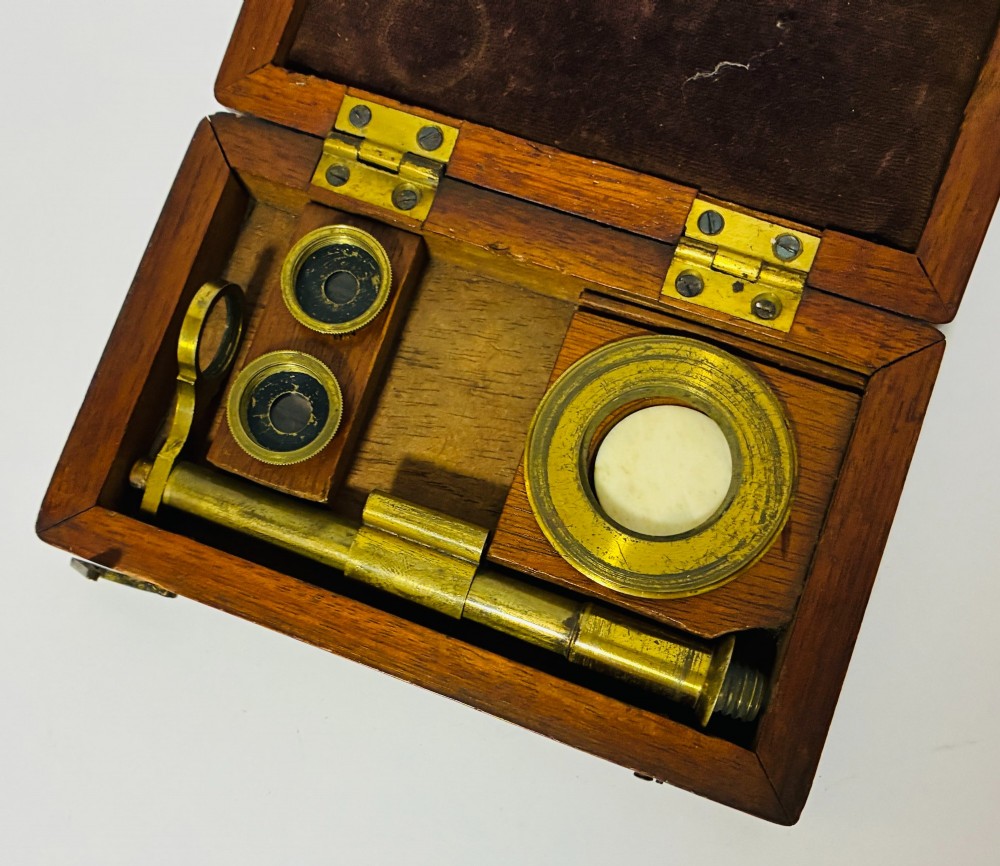 A 19th-century brass botanical field microscope mounted upright on a polished mahogany wooden storage box base. View VIII