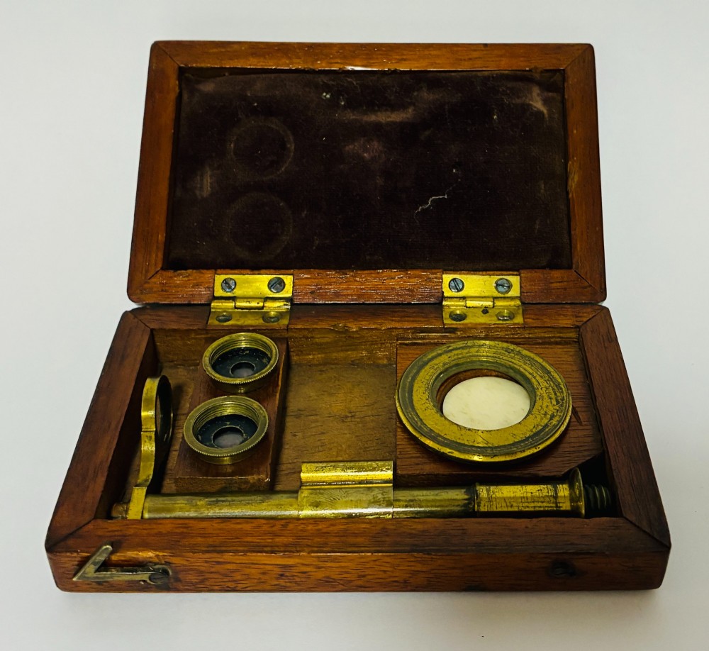 A 19th-century brass botanical field microscope mounted upright on a polished mahogany wooden storage box base. View IX