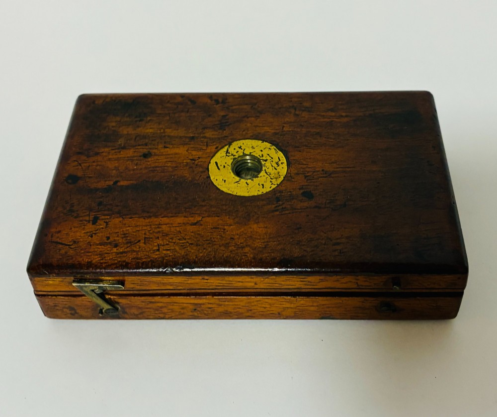 A 19th-century brass botanical field microscope mounted upright on a polished mahogany wooden storage box base. View X