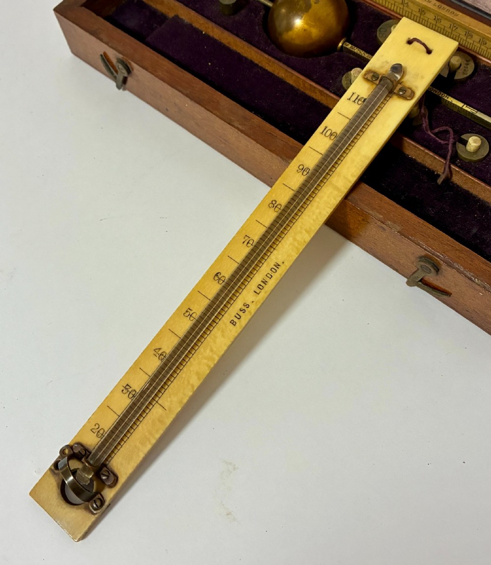 A Victorian Sikes hydrometer set resting inside an open fitted mahogany box lined with purple velvet, containing a brass float, slotted weights, and a thermometer. View VII